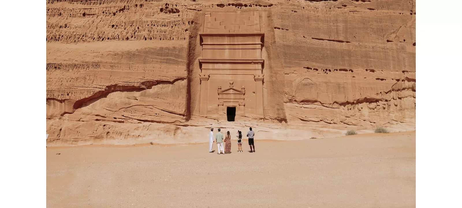 Visitors standing before a rock-cut tomb at Hegra